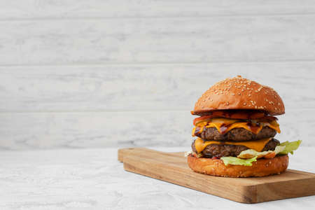 Double cheeseburger served on wooden board against white blurred backgroundの写真素材