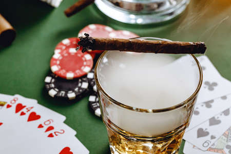 Glass of whiskey, cigar, playing cards and chips on green background