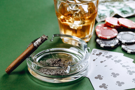 Glass of whiskey, cigar, playing cards and chips on green background