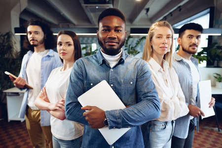 Group portrait of five diverse young colleagues standing in a row in office