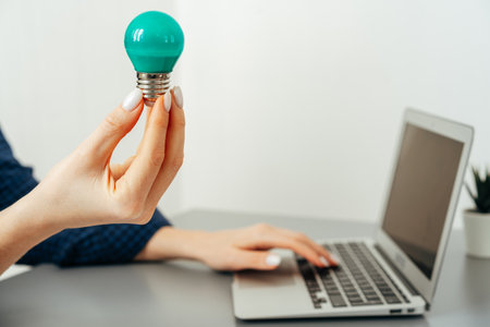 Female hand holding a light bulb above the tableの写真素材