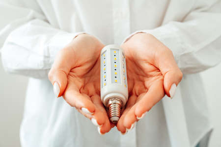 Woman in white shirt holding light bulb in hand