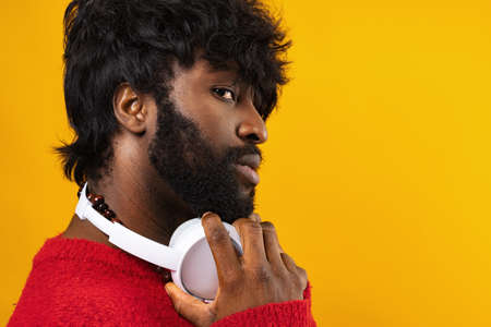 Young african american man with white headphones against yellow background