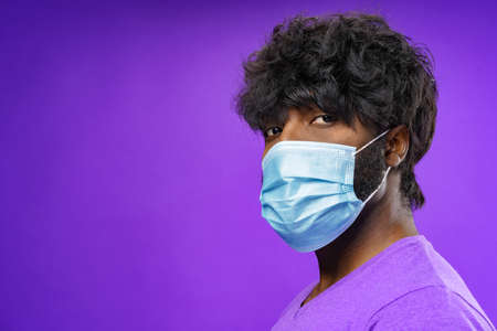 African american man wearing medical face mask against purple backgroundの写真素材