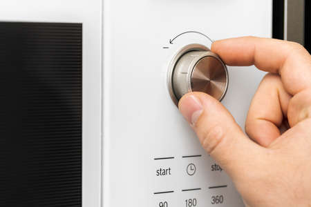Hand pushing button of microwave oven for cooking food in kitchenの写真素材