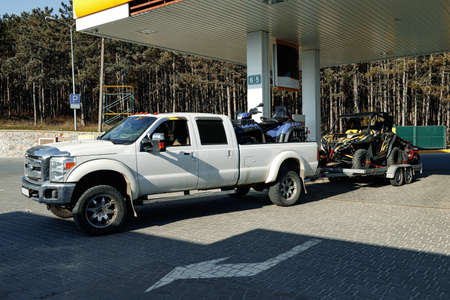 White pick-up truck loaded with ATV near gas station