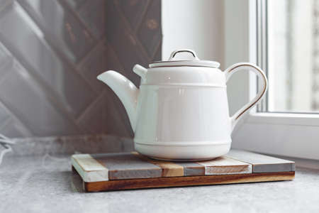 White ceramic teapot on wooden board on kitchen countertopの写真素材