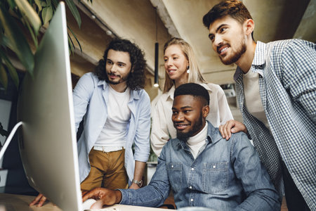 Four multiethnic colleagues looking at computer screen in officeの写真素材