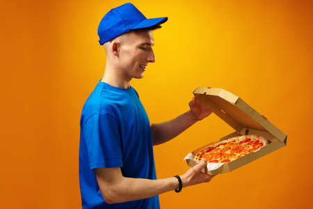 Happy young delivery man holding pizza box against yellow backgroundの写真素材