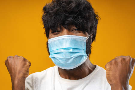 Positive handsome african american man with medical mask against yellow backgroundの写真素材