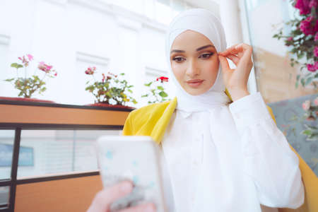Young muslim woman in hijab using her smartphone in cafeの写真素材