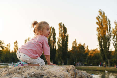 Little girl sitting on a huge stone in park near the lakeの写真素材