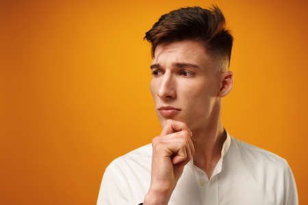 Portrait of thoughtful young man who looks away touching his chinの写真素材