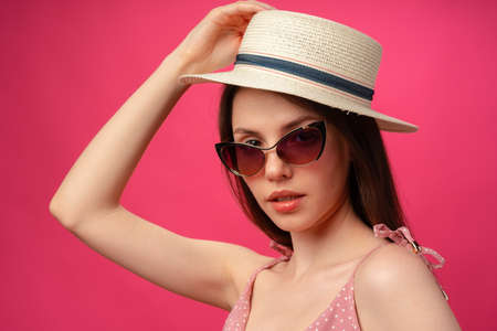 Studio fashion portrait of a young attractive woman in hat and glasses against pink backgorundの写真素材