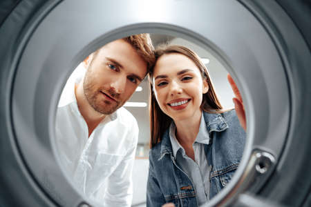 Happy couple choosing new washing machine in a store, view from the inside of washing machineの写真素材