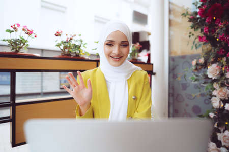 Beautiful young muslim woman using laptop while sitting in cafeの写真素材