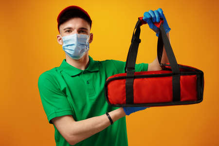 Young man courier in face mask with thermo bag