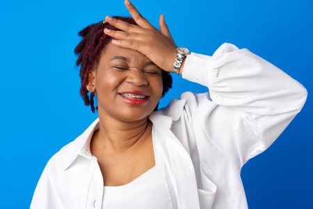 Young afro woman suffering headache against blue backgroundの写真素材