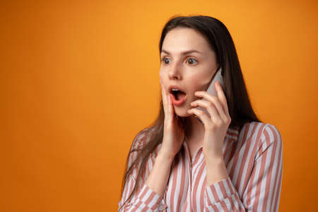 Studio photo of young woman talking on the phone against yellow background