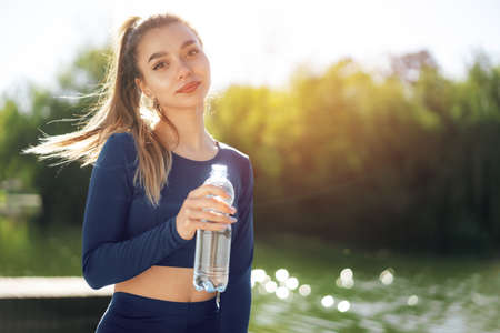 Portrait of young beautiful woman wearing blue sportswear drinking water at parkの写真素材