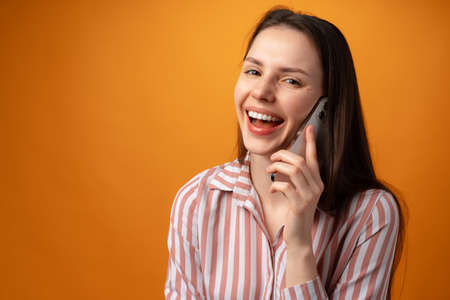 Studio photo of young woman talking on the phone against yellow backgroundの写真素材