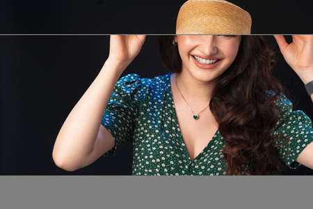 Beautiful young woman with straw hat posing against black background