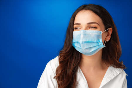 Young beautiful brunette woman wearing medical face mask against blue background