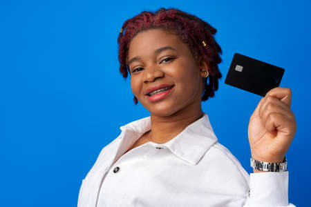 Young african american woman holding black credit card against blue backgroundの写真素材