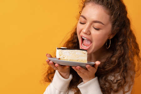 Young fit curly woman holding a piece of cake against yellow backgroundの写真素材