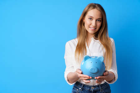 Beautiful smiling young woman with piggy bank on blue backgroundの写真素材