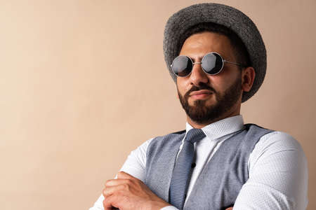 Cool egyptian man in hat and sunglasses posing against beige background