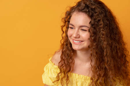 Portrait of a young curly-haired woman against yellow backgroundの写真素材