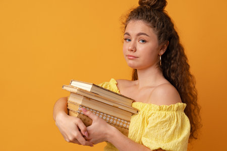 Young curly woman student holding book against yellow background