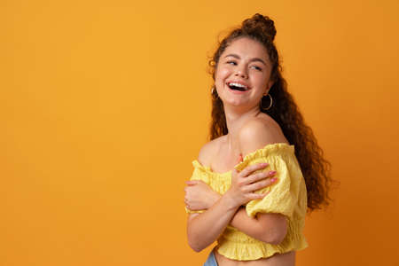 Portrait of a young curly-haired woman against yellow backgroundの写真素材