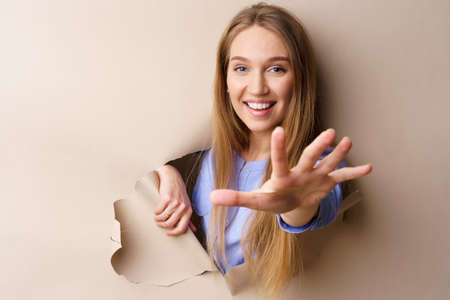 Beautiful young woman looking through a hole in beige paperの写真素材