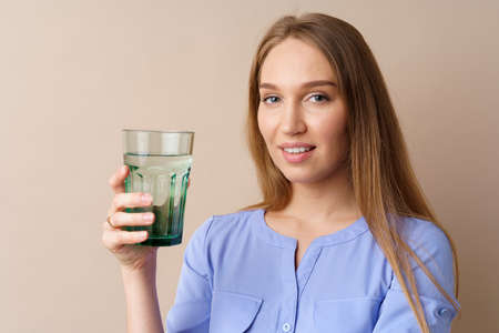 Beautiful healthy young woman drinking water from a glass on beige backgroundの写真素材