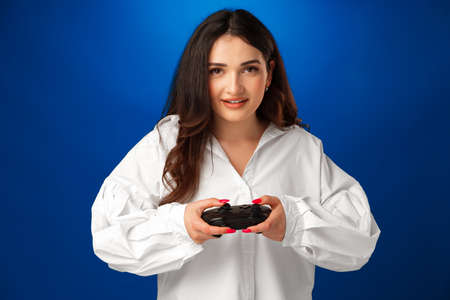 Beautiful brunette girl playing video games against blue background