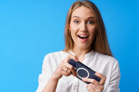 Positive young woman playing games on smartphone against blue background