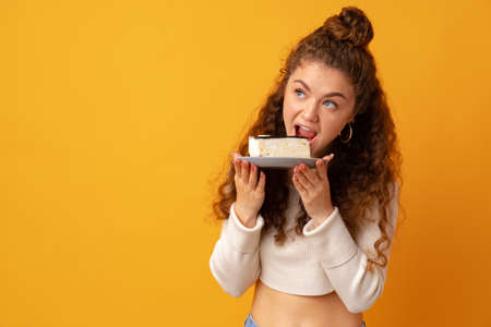 Young fit curly woman holding a piece of cake against yellow backgroundの写真素材