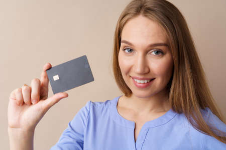 Beautiful young woman holding black credit card against beige background