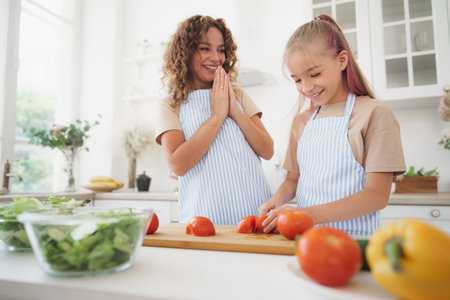 Mommy teaching her teen daughter to cook vegetable salad in kitchenの写真素材