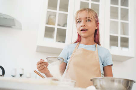 Portrait of a little blonde teen girl wearing apron in kitchen