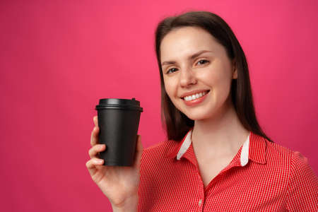 Portrait of attractive young woman with coffee cup against pink backgroundの写真素材