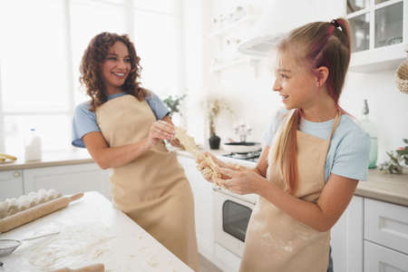 Teen girl helping her mom to cook dough in their kitchen at homeの写真素材