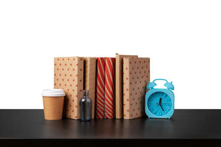 Alarm clock, stack of books and cup on tabletop against white backgroundの写真素材