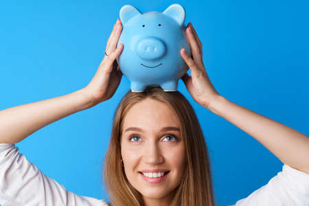 Beautiful smiling young woman with piggy bank on blue backgroundの写真素材