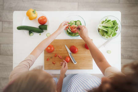 Close up of a woman and girl cutting vegetables for salad in kitchenの写真素材