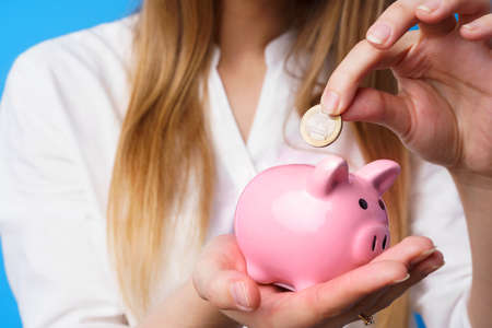 Female putting money into pink piggy bank against blue backgroundの写真素材