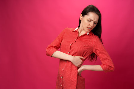 Brunette girl got back pain against pink backgroundの写真素材
