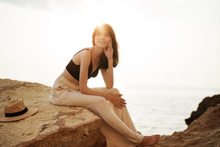Woman traveler sitting near sea on cliff injoying view of sea and nature